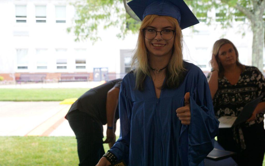 woman with glasses in a graduation cap and gown giving a thumbs up