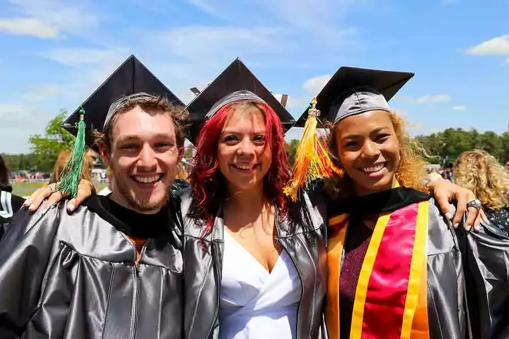 Three students smiling dressed in graduation caps and gowns.